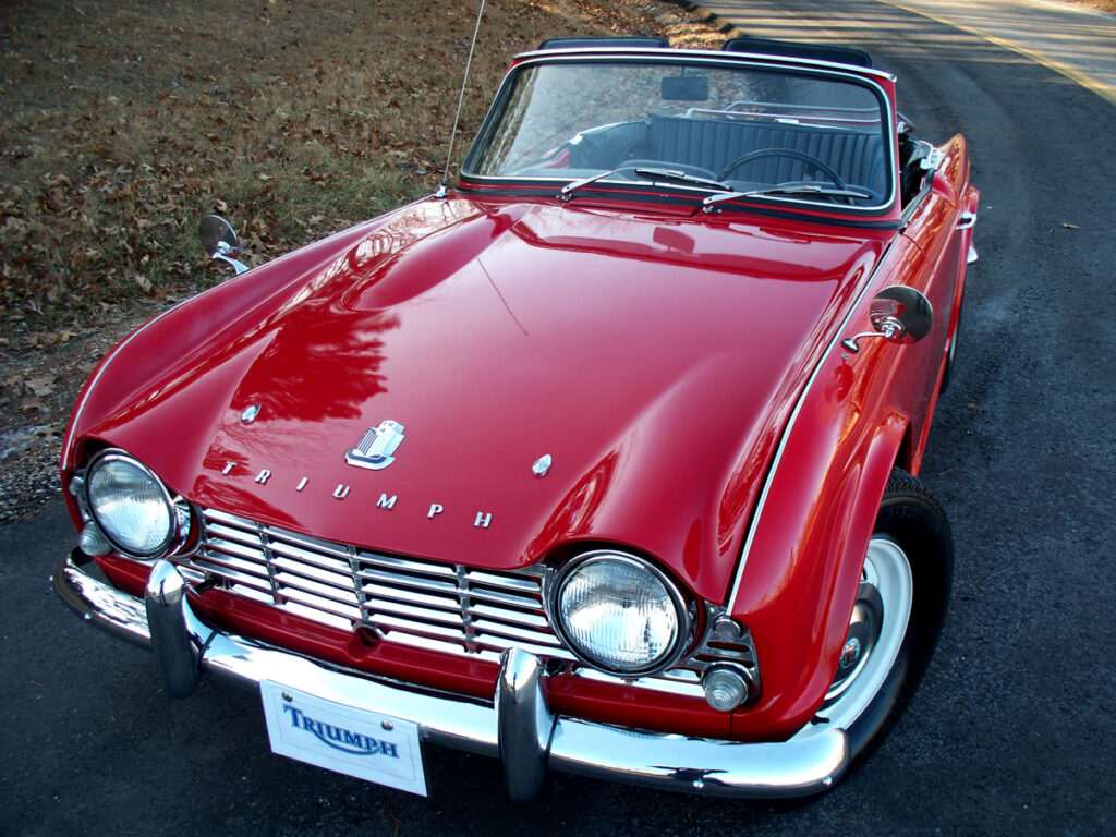 Triumph TR4 Der Triumph TR4 ist kein komfortabler Cruiser, sondern ein puristischer Fahrerwagen. Ohne Servolenkung oder elektronische Helfer bietet er ein unmittelbares, authentisches Fahrgefühl. Das große Drehmoment des Vierzylinders sorgt schon bei niedrigen Drehzahlen für kräftigen Vortrieb, während das knackige Getriebe mit Overdrive auf der Landstraße pure Freude bereitet. Mit gut eingestellter Achsgeometrie und modernen Reifen fährt sich der TR4 überraschend neutral. Wichtig ist, dass die Fahrwerksbuchsen und Stoßdämpfer in gutem Zustand sind – hier entscheidet sich, ob der Wagen sportlich oder schwammig wirkt.